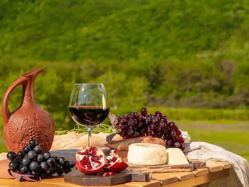 Yeşil çimenlerle kaplı bir çayırda, kırmızı şarap, peynir, meyve, üzüm ve ekmekle donatılmış bir masa